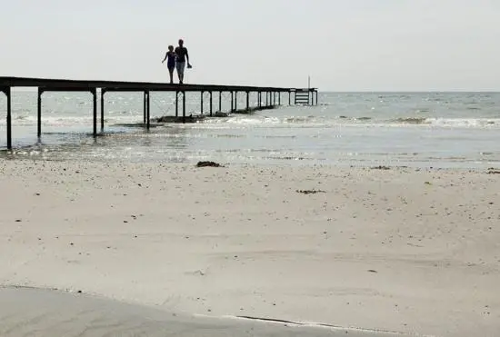 Strand, hav, horisont och en brygga med två personer.