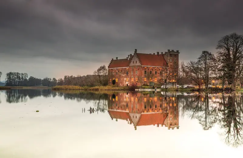 Bild på Svaneholms slott som speglar sig i sjön.