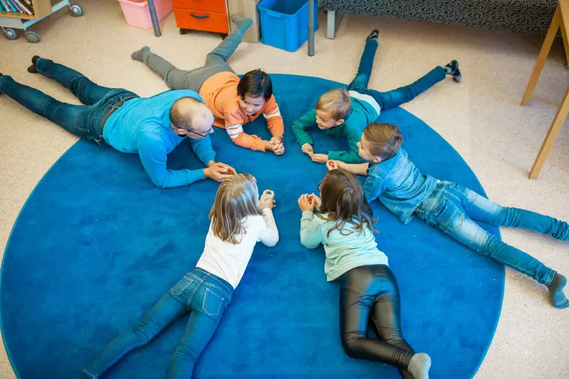 pedagog och elever ligger i en ring på en stor blå matta